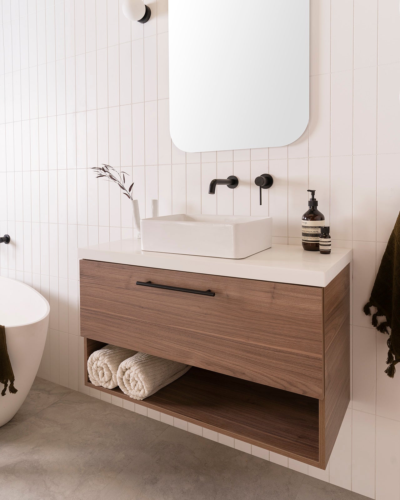 Glacier Ensuite Shelf, Slim 900 Centre Bowl. Notaio Walnut Ravine cabinet finish with Matte Black Round Cross Bar handle. 40mm Bright White Cherry Pie benchtop and Selma above-counter basin. 600mm Stadium Mirror. Soul Groove Wall Mixer and Spout in Matte Black.