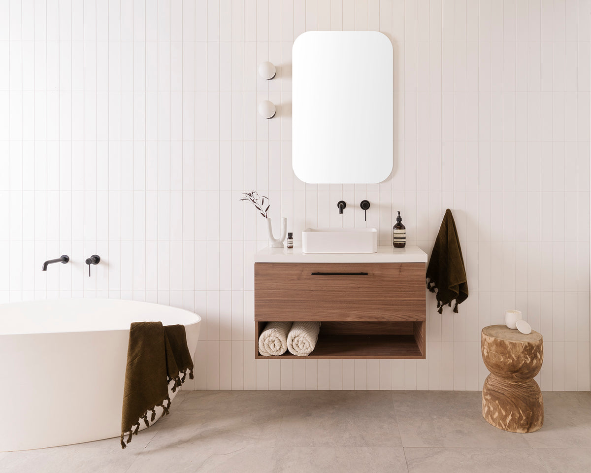 Glacier Ensuite Shelf, Slim 900 Centre Bowl. Notaio Walnut Ravine cabinet finish with Matte Black Round Cross Bar handle. 40mm Bright White Cherry Pie benchtop and Selma above-counter basin. 600mm Stadium Mirror. Soul Groove Wall Mixer and Spout in Matte Black.